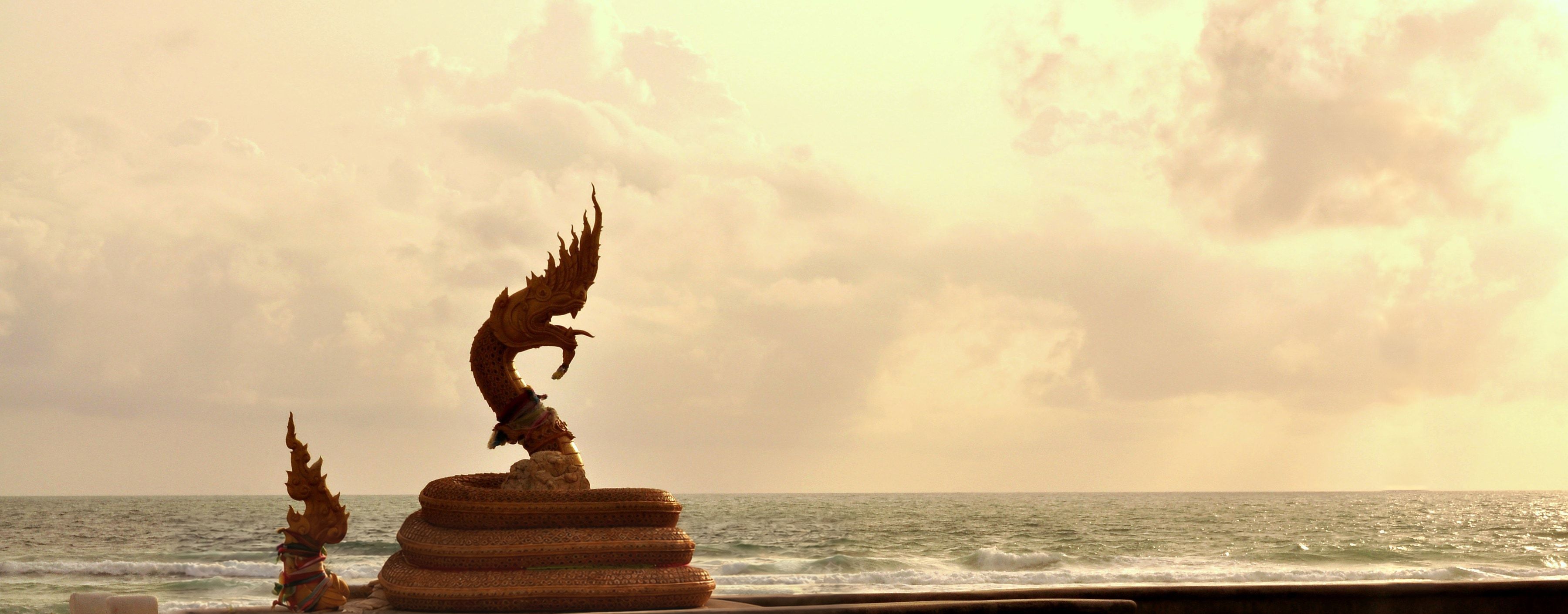 The golden naga statue on Karon Beach at sunset