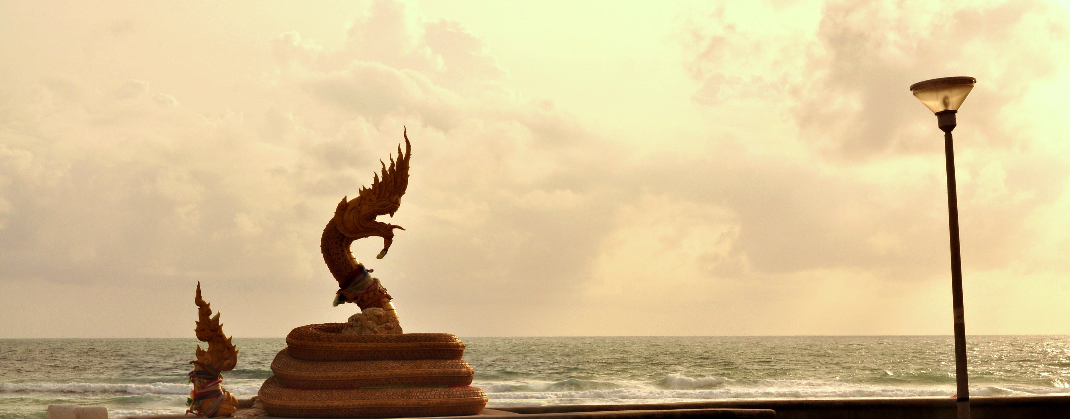 The golden naga statue on Karon Beach at sunset